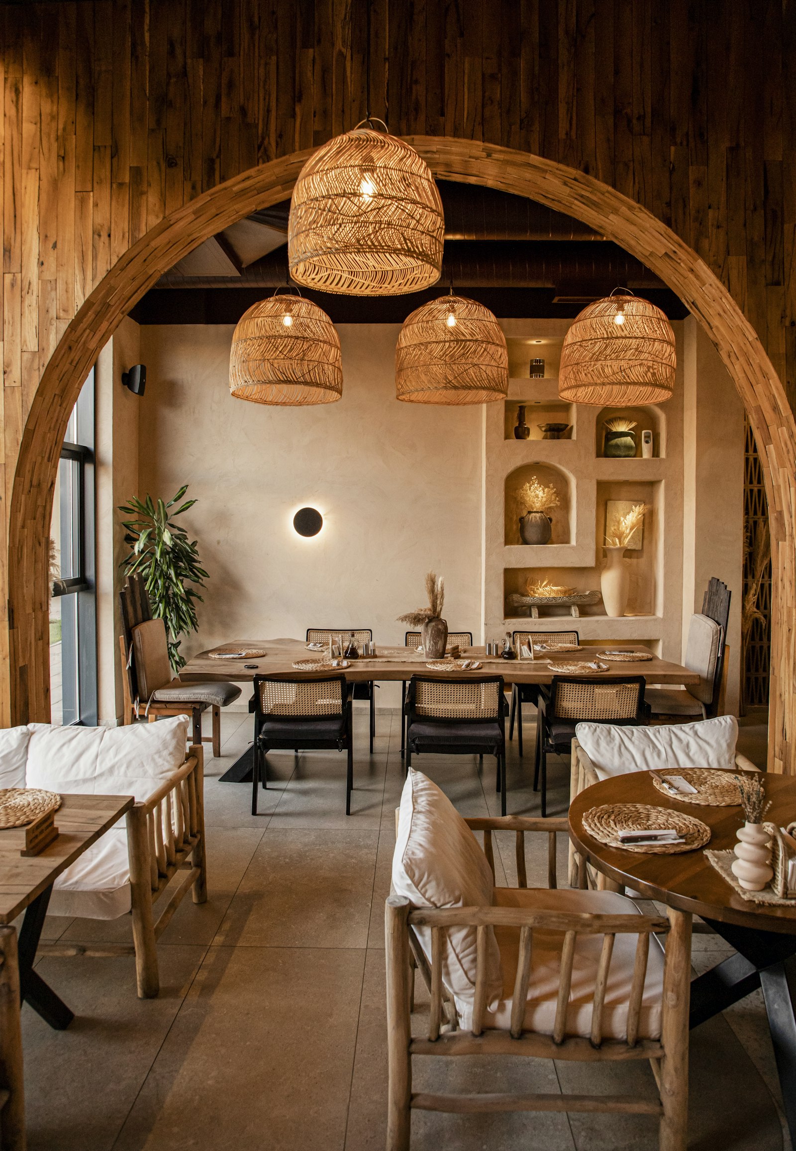 Salle à manger sous une arche en bois, suspensions en rotin